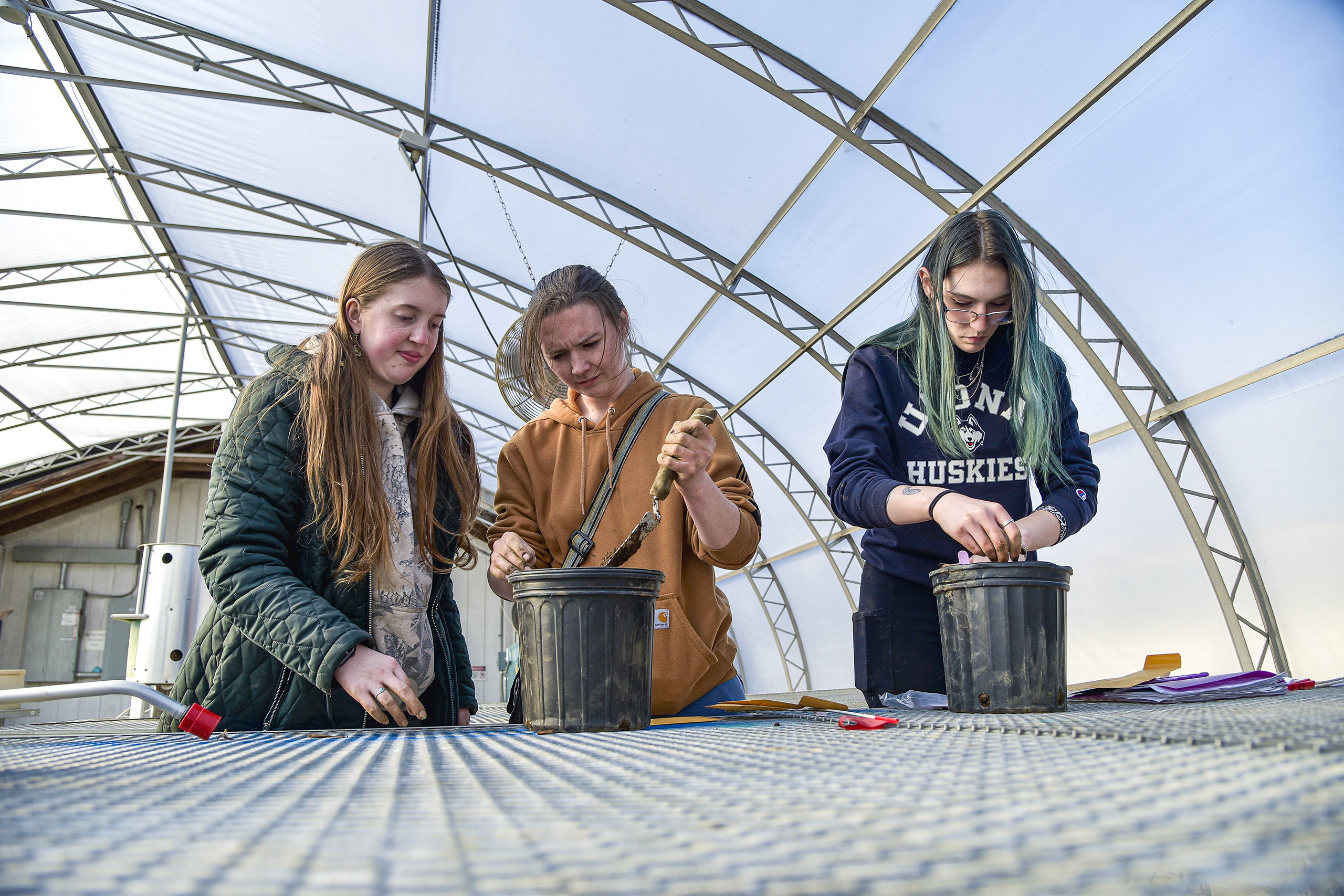 three students filling pots with soil in a greenhouse