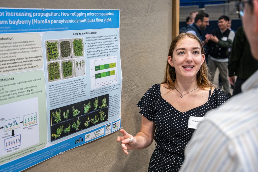 student standing. in front of research poster and discussing with another person